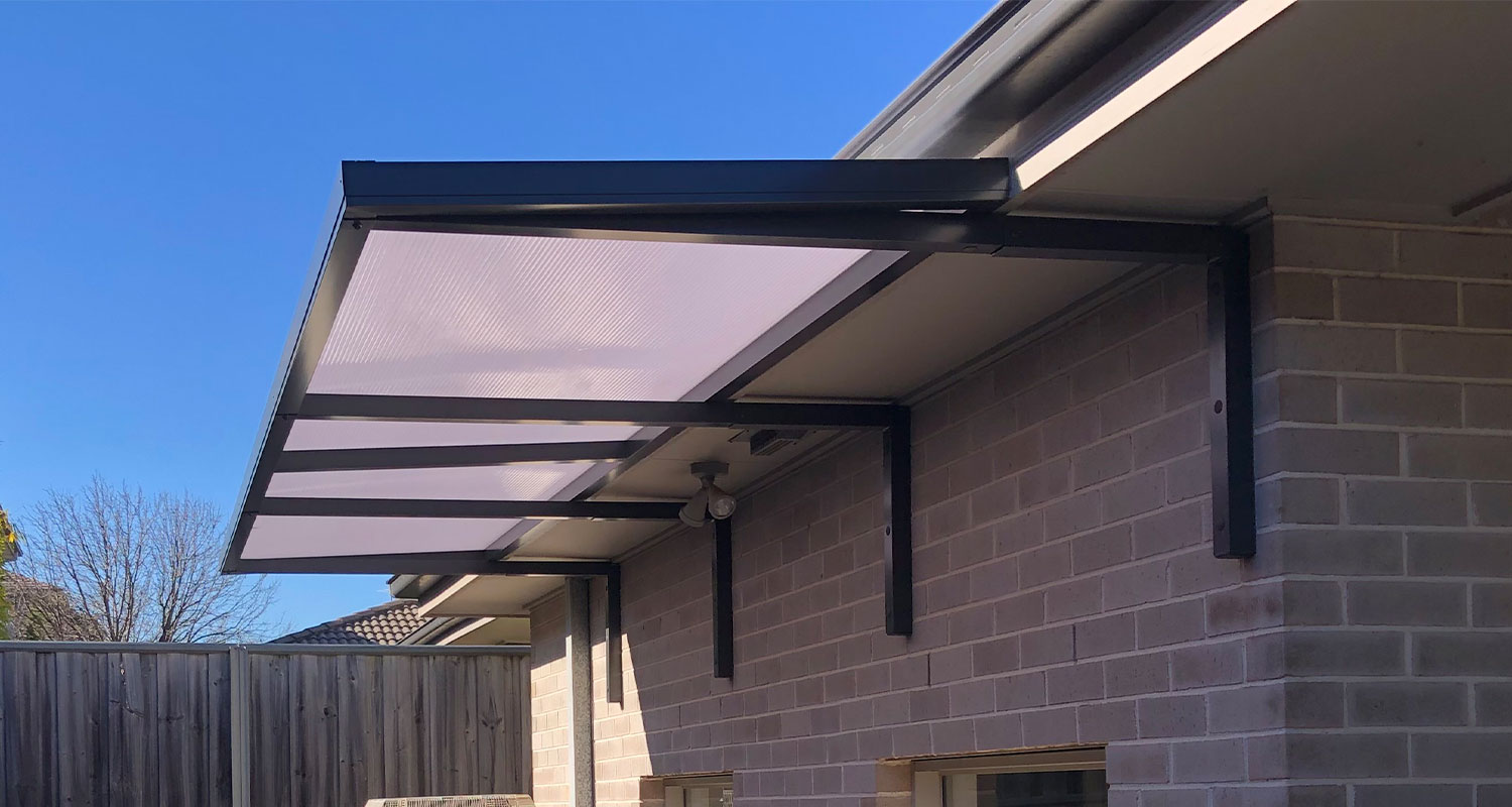 Slimline 50 under-eave awning with polycarbonate roof and front posts, dark grey frame, large span on Sydney brick home