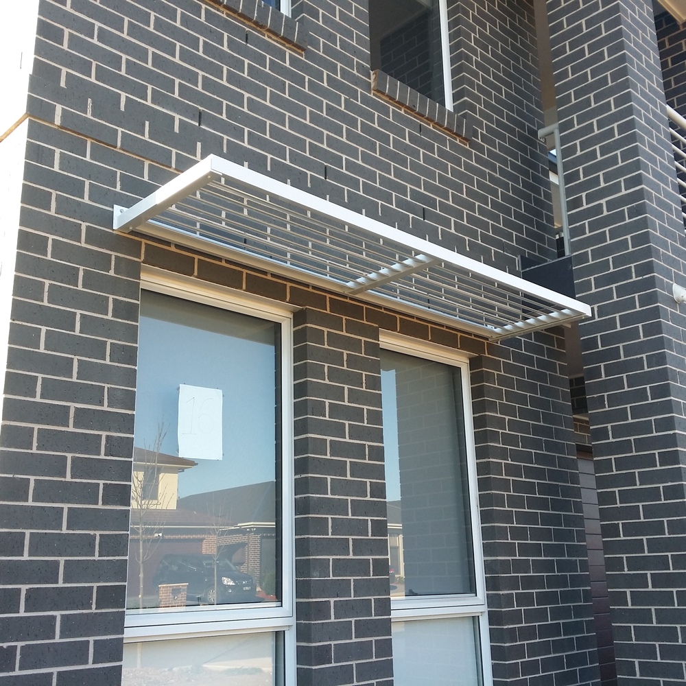 Cantilever aluminium louvre awning mounted to a brick wall above windows for sun shading and airflow control