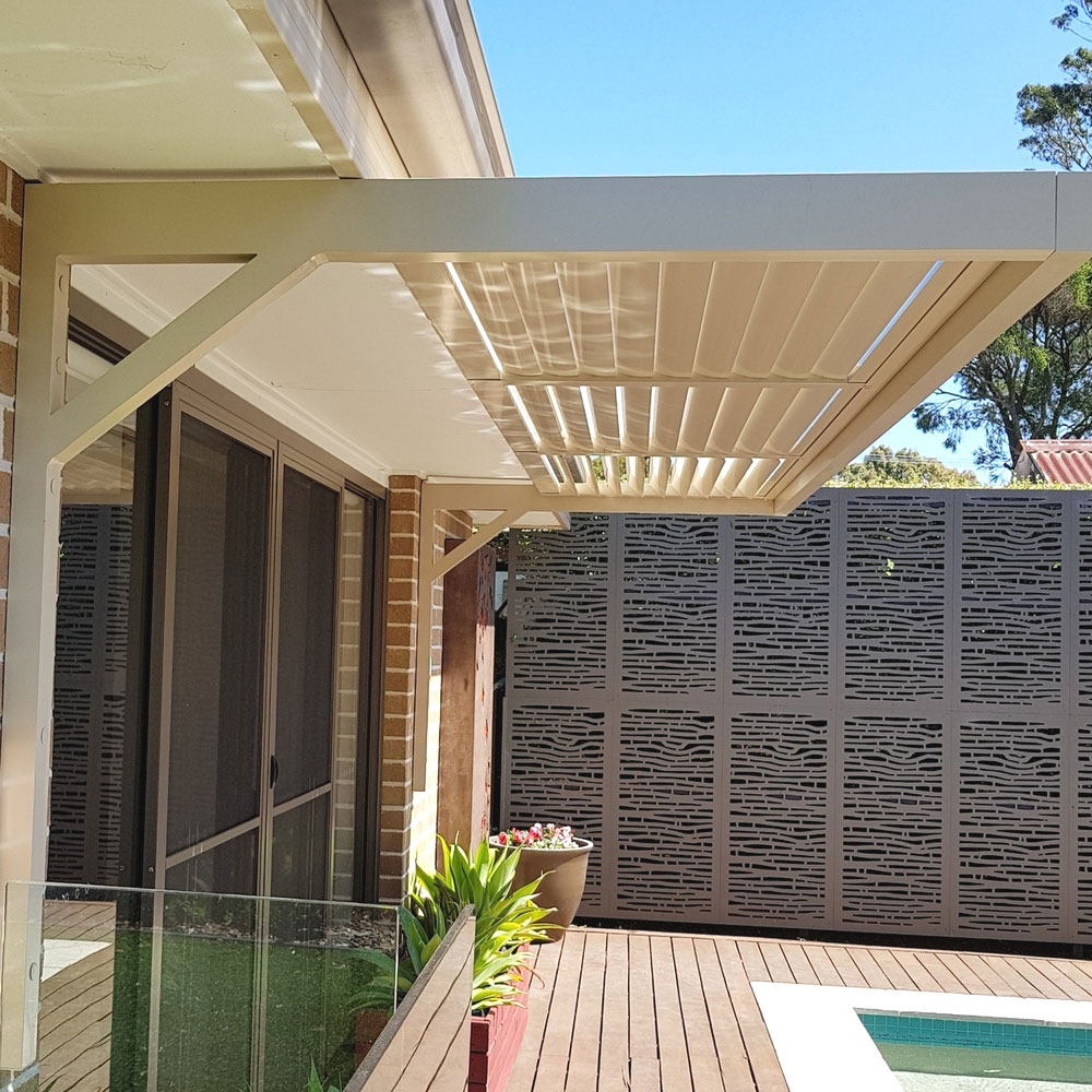 Cantilever aluminium louvre awning with heavy-duty frame installed under an eave above sliding doors beside a pool deck.