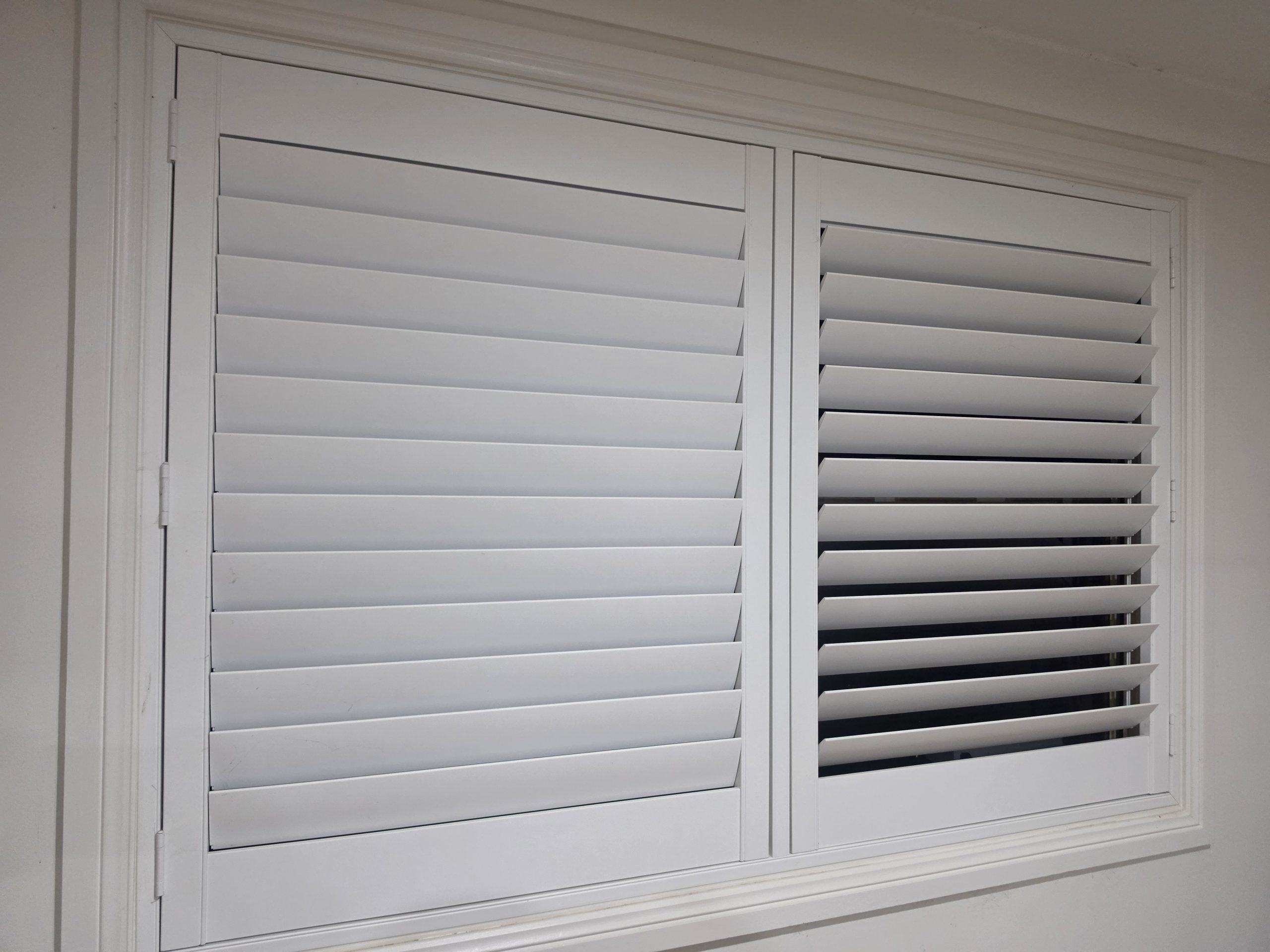 plantation shutters with one panel of blades closed and one open, showing indoor light control